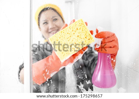 Happy housewife staying inside shower and cleaning it with yellow sponge.