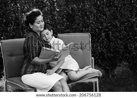 Loving mother is reading book for her son in their garden.
