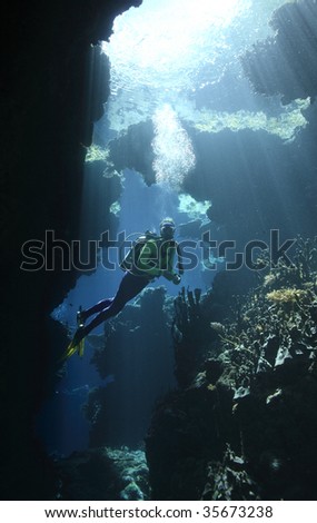 a female scuba diver in an underwater cave with sunbeams shining through the water