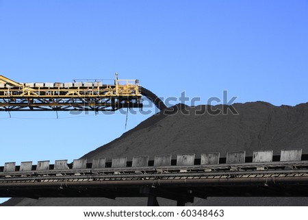 a large yellow conveyor belt carrying coal and emptying onto a huge pile.