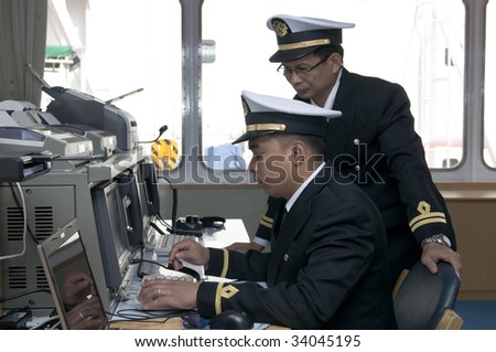 Navigation officers manage devices, looking ahead on the navigation bridge of ocean ship