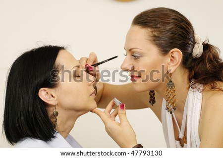 Beautician master is doing make-up to model girl