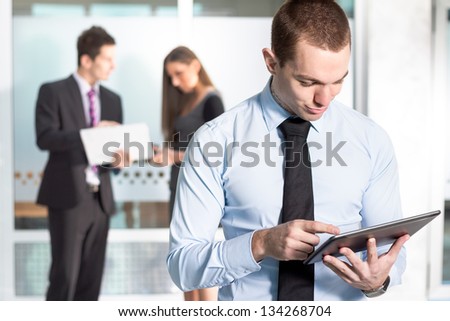 Portrait of young business man working on digital tablet with executives in the background