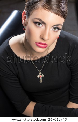 Elegant beautiful woman in a black cocktail dress and long gloves wearing cross necklace
