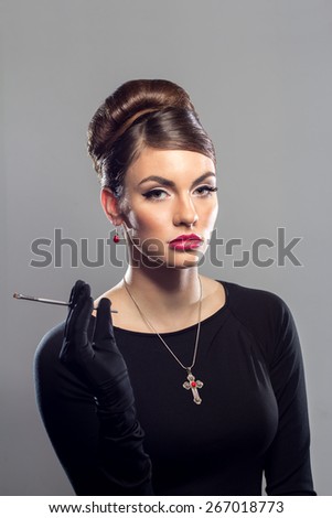 Portrait of young woman in black dress holding a makeup brush on a grey background