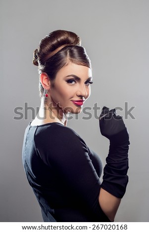 Elegant beautiful woman in a black cocktail dress and long gloves looking at camera
