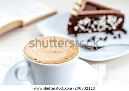 Coffee cup with a chocolate cake and a book in the background