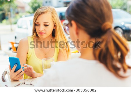 Young girl sitting in the cafe with a friend and using mobile phone