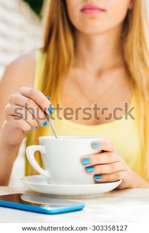Young girl with a long blond hair stirring coffee