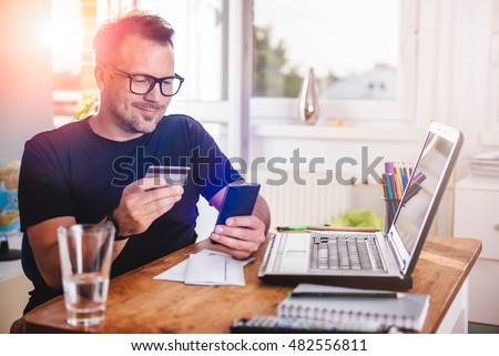 Man paying with credit card on smart phone at home office