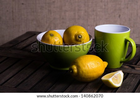 Fresh tangy yellow lemons in a green ceramic bowl with a matching mug of tea and cut quarter fruit in the foreground