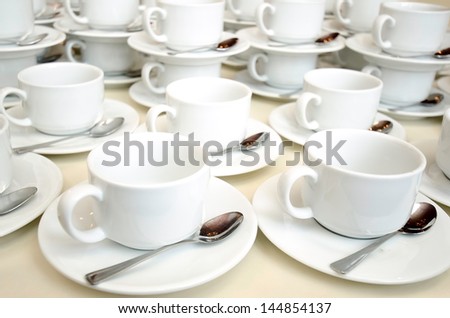 White ceramic cups and saucers laid out on a buffet table at a catered event for serving a hot beverage