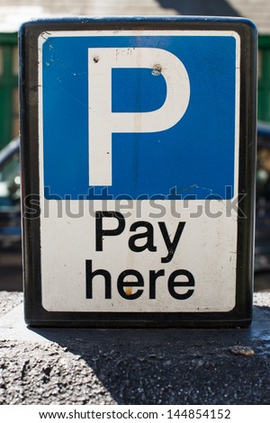 Pay Here signboard on top of an exterior wall with parked cars visible behind, closeup view