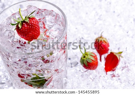 Iced drink with ripe strawberries and crushed ice in a glass standing on a bed of crushed ice with further strawberries below