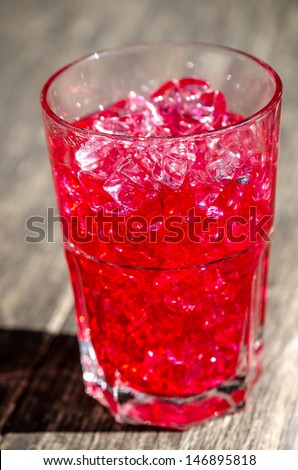 Glass tumbler of ice cold red soda or cocktail served with crushed ice for a refreshing drink on a hot summer day standing outdoors in the sunshine on a wooden table