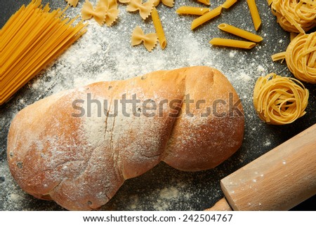 Delicous traditional italian white bread ciabatta and rolling pin with various types of pasta -  tagliatelle, spaghetti, rigatoni, bows on floury black backround
