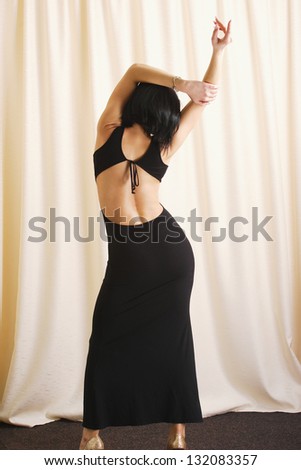 Young girl with black dress against home curtains. back to the camera