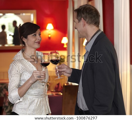 Romantic smiling couple toasting each other with red wine in a plush red interior