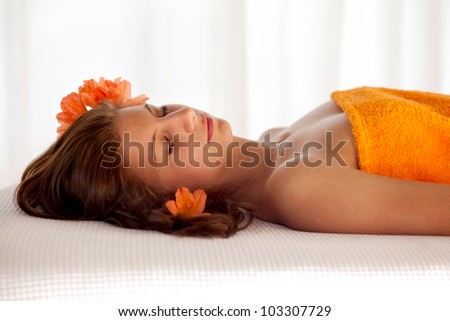 Beautiful young woman in a state of total relaxation and well being lying with her eyes closed on a spa table draped in an orange towel with orange blossoms in her hair
