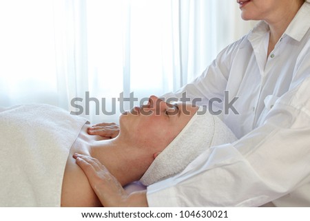 Woman with a white towel around her head relaxing on a table in a spa while a female therapist massages her shoulders during treatment