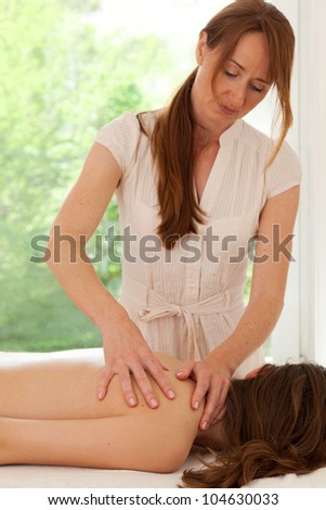 Female alternative practitioner giving a back massage to her client backed by a window looking on to foliage with copy-space