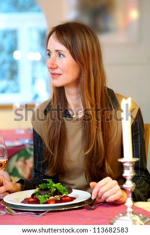Fashionable attractive mature woman dining out by candlelight in a restaurant with a serving of food on a plate in front of her