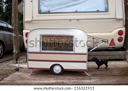 Tiny model caravan for a small pet dog parked at the back of the owners full size caravan in a campsite.