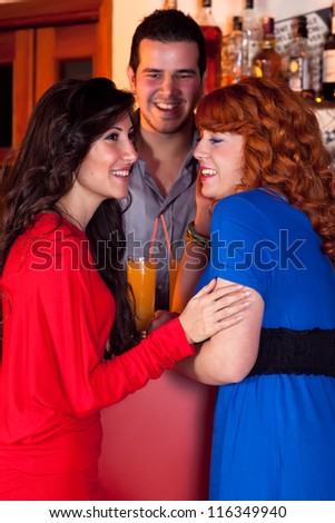 Three friends at a bar laughing together at a joke with two fashionable woman in profile touching in the foreground and a young man behind.