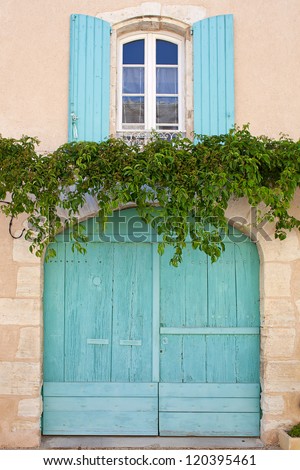 Wooden window and garage door with rounded top, turquoise painted, ivy tendrils among. France, Provence