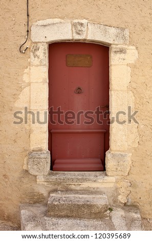 Old restored red painted entrance door, with ancient steps in front, leading to an antique house. Provence, France.