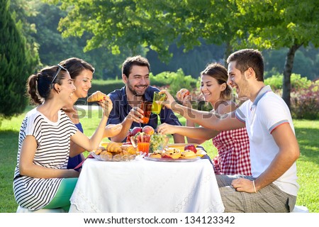 Friends enjoying a relaxing picnic sitting together laughing and chatting at a table in a lush green park