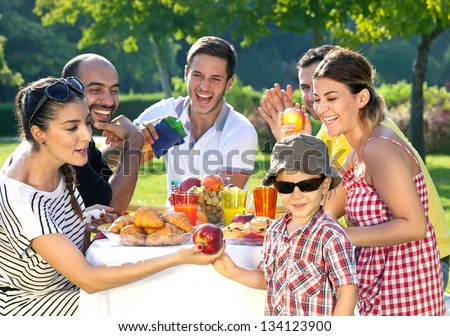 Multi Ethnic Group Of Friends Enjoying A Meal Together Outdoors In The Garden With A Small Boy In Sunglasses In The Foreground