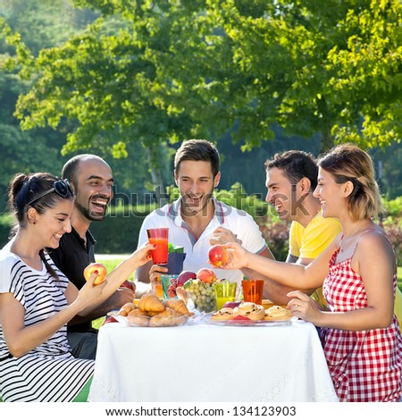 Picnic. Multi ethnic friends sharing an enjoyable meal seated at a table outdoors in the garden laughing and joking together