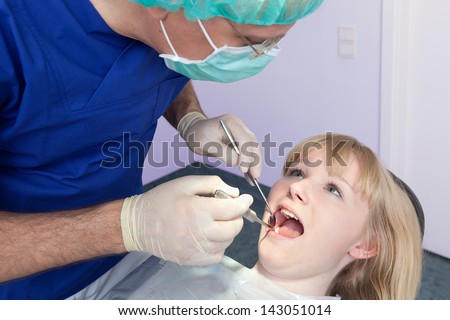 Dental-Surgeon examining the teeth of a woman. Dental-Surgeon using a mask and cap performing an examination of the teeth on a beautiful blond woman