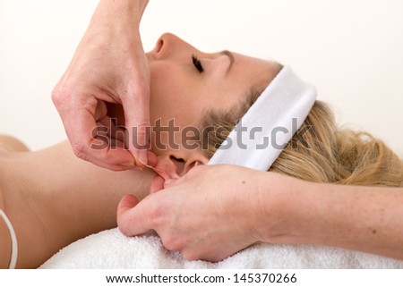 Homeopath applying an acupuncture needle on ear. Alternative practitioner applying an acupuncture needle on the earlobe of a beautiful and relaxed blond woman
