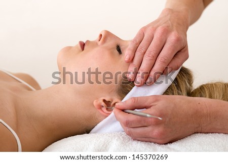 Chiropractor applying ear acupuncture techniques. Homeopath applying ear acupuncture techniques also called auriculotherapy on the earlobe of a beautiful blond woman while holding her forehead