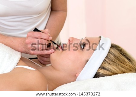 Make-up artist applying lipstick on a woman. Make-up artist applying lipstick with a brush on a beautiful laid down blond woman