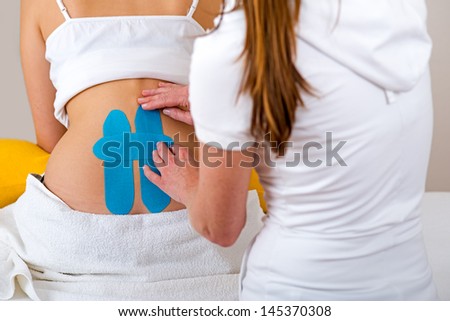 Chiropractor applying three kinesiology tapes. Chiropractor applying two kinesiology tapes to the back of a woman for pain relieve