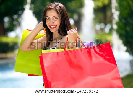Young female beauty with full of huge shopping bags, in front of fountains along a shopping mall.