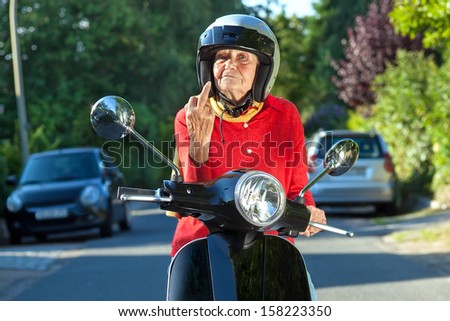 Angry old lady on a scooter making a rude gesture. Senior woman showing the finger while sitting on a scooter bike in a sign of road rage