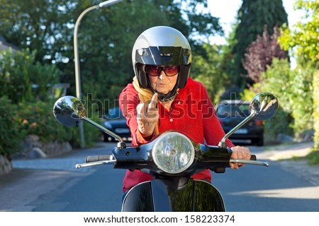 Crotchety old lady on a scooter making a rude gesture of dismissal with her finger as she sits looking over the hand bars with a disdainful expression