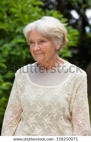 Portrait of a thoughtful elderly woman. Portrait of a thoughtful elderly grey haired woman standing in the sunshine in a park staring into the distance as she reminisces old memories