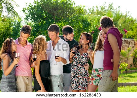 Group of young teenage college friends socializing enjoying a glass of red wine together while standing chatting in the garden
