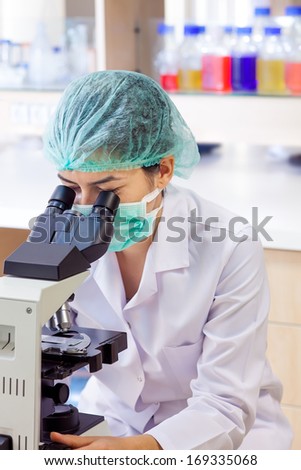 Laboratory technologist or technician using a microscope analyzing a slide while wearing a surgical cap and mask