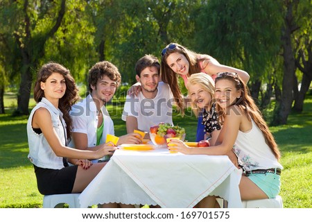 Group of college friends posing for the camera sitting together relaxing on a summer day enjoying a picnic in the park during their vacation.