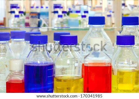 Colourful chemical solutions for conducting experiments in a laboratory standing in rows of clear glass bottles, close up background view.