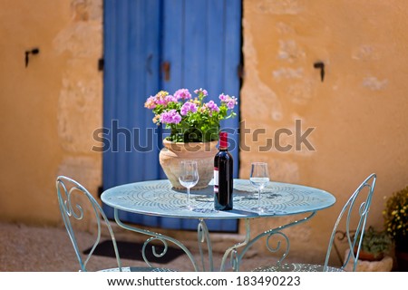 Table for two set with red wine in front of a rustic country house. The wall is painted in ochre with wooden door in blue.