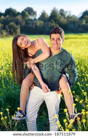 Two attractive laughing young lovers in a field of yellow rapeseed with the man giving his girlfriend a piggy back ride as they enjoy nature together