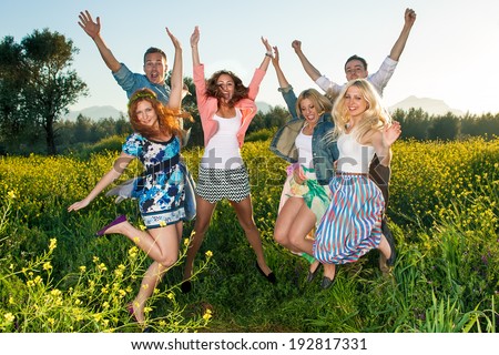 Group of excited young people leaping in the air and celebrating a beautiful hot sunny summer day as they enjoy an outing into the countryside in a colorful yellow rapeseed field