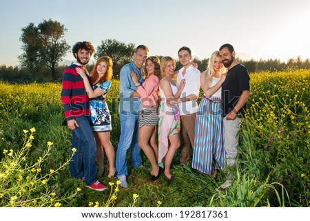 Four romantic affectionate young couples standing grouped together in the country at sunset as they enjoy a relaxing evening together in nature in a yellow rapeseed field